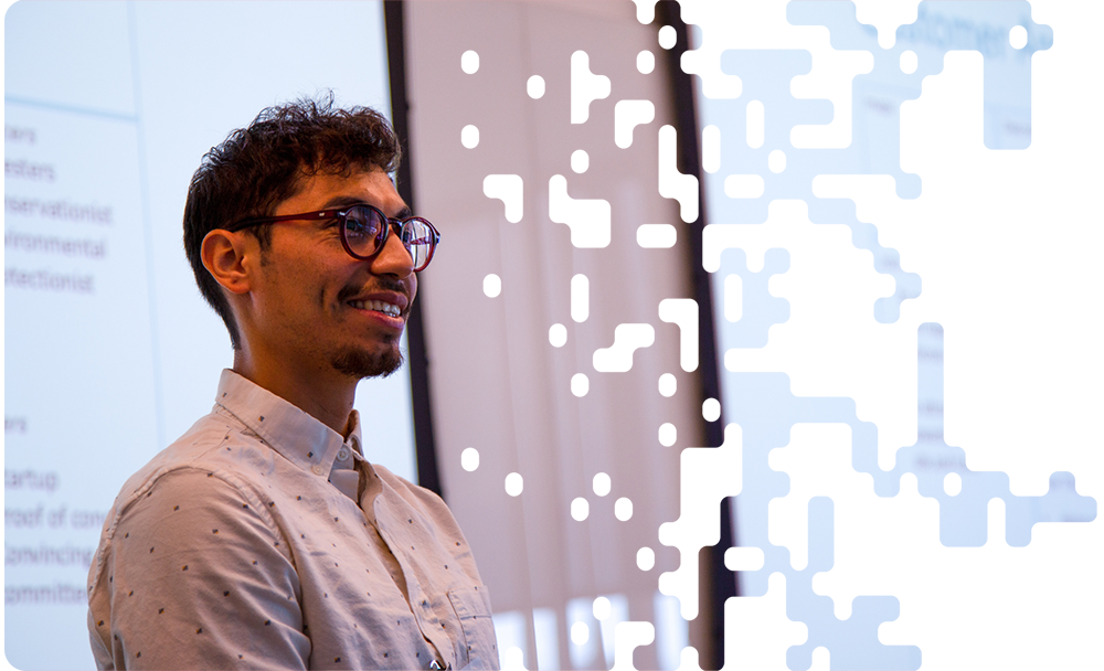 A young male entrepreneur with glasses smiles while giving a presentation