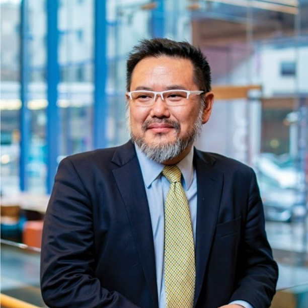 Shintaro Kaido, an I-Corps mentor with a beard and white glasses, smiles in a suit