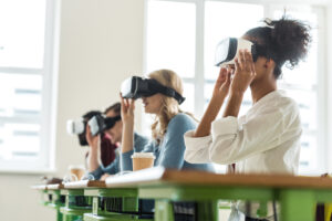 Four individuals sitting at desks and wearing virtual reality headsets.