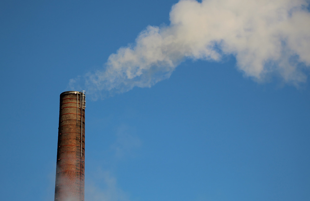 A smokestack billows smoke against a blue sky.